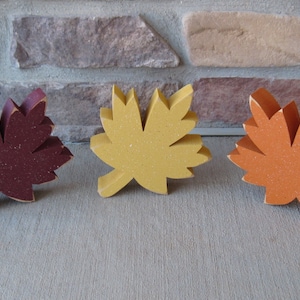K&ouml;nnte beinhalten: Drei h&ouml;lzerne Herbstbl&auml;tter in verschiedenen Farben: Rotbraun, Gelb und Orange. Die Bl&auml;tter sind alle gleich gro&szlig; und gleich geformt und in einer Reihe angeordnet.
