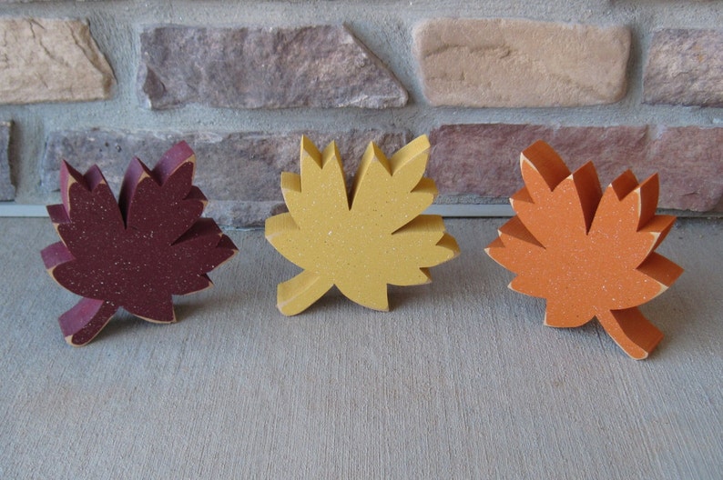 K&ouml;nnte beinhalten: Drei h&ouml;lzerne Herbstbl&auml;tter in verschiedenen Farben: Rotbraun, Gelb und Orange. Die Bl&auml;tter sind alle gleich gro&szlig; und gleich geformt und in einer Reihe angeordnet.