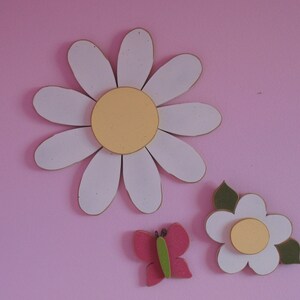 May include: Three white paper daisies with yellow centres and a pink butterfly on a pink background.