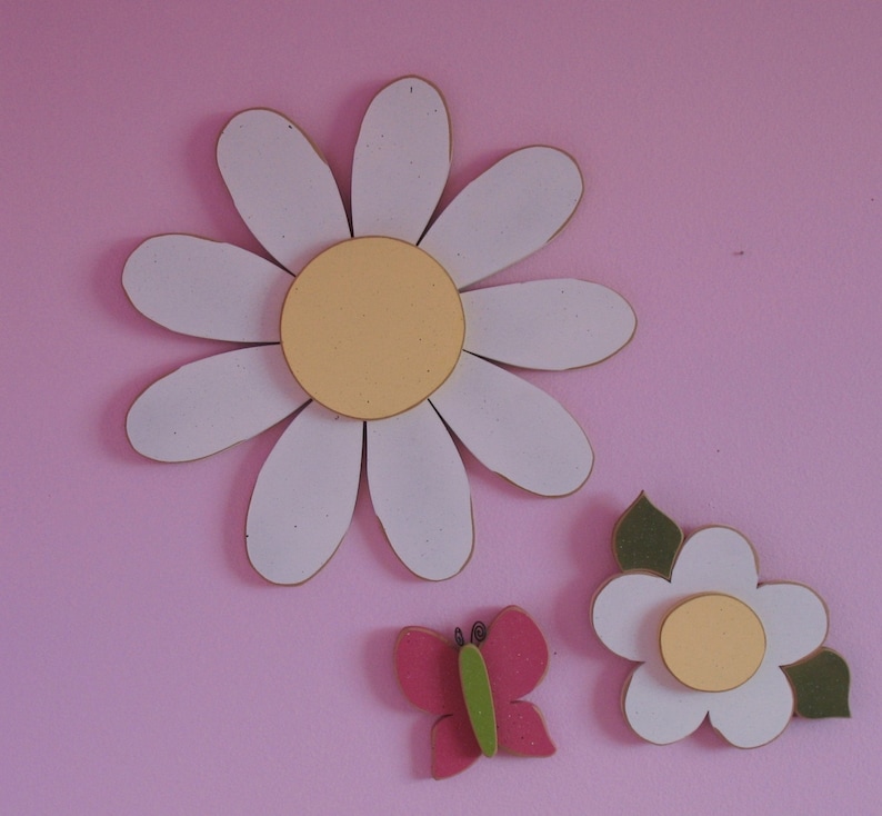 May include: Three white paper daisies with yellow centres and a pink butterfly on a pink background.