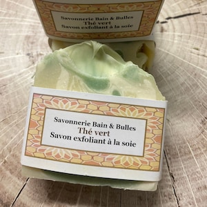 May include: Two bars of green tea scented soap with a white and green swirl pattern. The soap is wrapped in a label that reads "Savonnerie Bain & Bulles Th&eacute; vert Savon exfoliant &agrave; la soie".