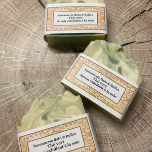 May include: Three bars of green and white soap with a label that reads "Savonnerie Bain & Bulles Th&eacute; vert Savon exfoliant &agrave; la soie".