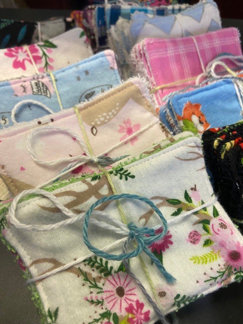 Op de afbeelding: Een stapel handgemaakte herbruikbare make-up remover pads in verschillende patronen, waaronder bloemen, ruitjes en geometrische ontwerpen. De pads zijn met touw aan elkaar gebonden en klaar voor gebruik.