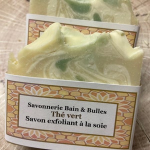 May include: A white and green bar of soap with a label that reads "Savonnerie Bain & Bulles Th&eacute; vert Savon exfoliant &agrave; la soie".