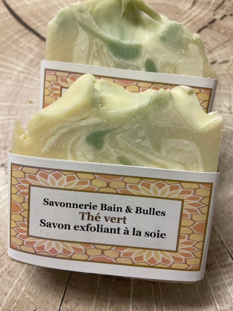 May include: A white and green bar of soap with a label that reads "Savonnerie Bain & Bulles Th&eacute; vert Savon exfoliant &agrave; la soie".