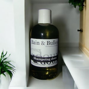 May include: A clear glass bottle of shampoo with a white label that reads "Bain & Bulles Savonnerie artisanale Cheveux Shampooing doux www.bainetbulles.com Ste-Julienne, QC".