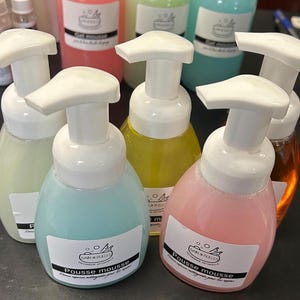May include: Five bottles of foaming hand soap in different colours. The bottles are labelled "Pousse mousse" and "Bain & Bulles".