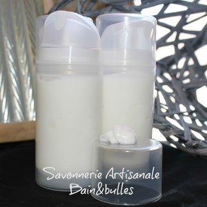 May include: Two clear plastic pump bottles filled with white cream, featuring a small dollop of cream on the detached cap. The text Savonnerie Artisanale Bain&bulles is printed in white across the lower portion of the bottles and the cap.