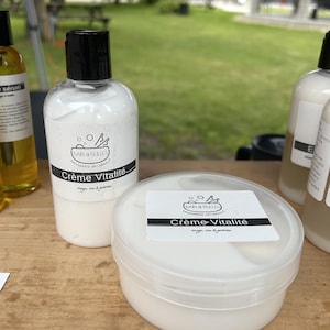 May include: A white cream product in a clear plastic squeeze bottle and a matching white cream in a round, clear plastic tub. Both containers feature a white label with the text Bain & Bulles Savonnerie Artisanale Cr&egrave;me Vitalit&eacute;.