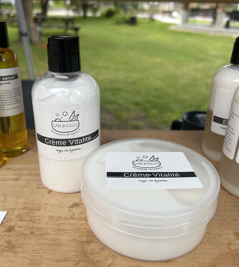 May include: A white cream product in a clear plastic squeeze bottle and a matching white cream in a round, clear plastic tub. Both containers feature a white label with the text Bain & Bulles Savonnerie Artisanale Cr&egrave;me Vitalit&eacute;.