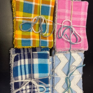 Op de afbeelding: Vier stapels stofvierkanten gebonden met touw. De vierkanten hebben verschillende patronen: geel en blauw ruitpatroon, roze ruitpatroon, blauw en wit ruitpatroon en wit met een blauw zigzagpatroon.