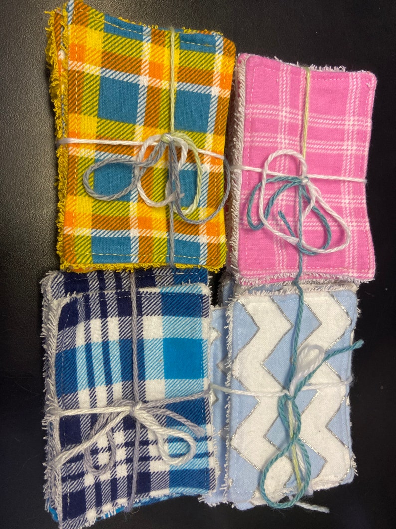 Op de afbeelding: Vier stapels stofvierkanten gebonden met touw. De vierkanten hebben verschillende patronen: geel en blauw ruitpatroon, roze ruitpatroon, blauw en wit ruitpatroon en wit met een blauw zigzagpatroon.