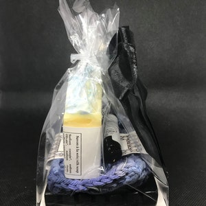 Puede incluir: Un set de regalo con una barra de jab&oacute;n, una peque&ntilde;a botella de l&iacute;quido y una cuerda trenzada azul y morada. Los art&iacute;culos est&aacute;n empaquetados en una bolsa de pl&aacute;stico transparente con una cinta negra.