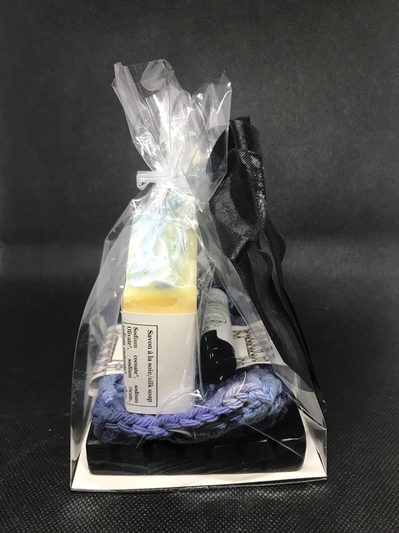 Puede incluir: Un set de regalo con una barra de jab&oacute;n, una peque&ntilde;a botella de l&iacute;quido y una cuerda trenzada azul y morada. Los art&iacute;culos est&aacute;n empaquetados en una bolsa de pl&aacute;stico transparente con una cinta negra.