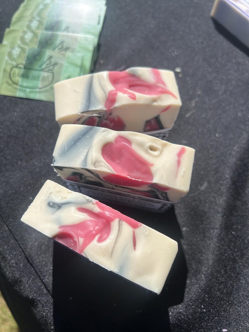 Puede incluir: Tres barras rectangulares de jab&oacute;n artesanal con un patr&oacute;n jaspeado de remolinos en color crema, gris carb&oacute;n y rosa vibrante. Las barras de jab&oacute;n tienen una textura suave y s&oacute;lida, y est&aacute;n dispuestas en una pila escalonada con una mezcla de colores uniforme.