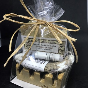 Puede incluir: Un set de regalo para el ba&ntilde;o y el cuerpo que incluye una pastilla de jab&oacute;n, un peque&ntilde;o tubo de loci&oacute;n, una toallita y un jabonera de madera. El jab&oacute;n est&aacute; envuelto en pl&aacute;stico transparente y atado con una cinta marr&oacute;n. El jab&oacute;n est&aacute; etiquetado con "Savonnerie Bain & Bulles Avoine et miel Savon &agrave; la soie". El tubo de loci&oacute;n est&aacute; etiquetado con "res ma beewax". La toallita es beige con un borde blanco. La jabonera est&aacute; hecha de madera marr&oacute;n claro y tiene las palabras "Le Ptit beis" grabadas en la parte inferior.