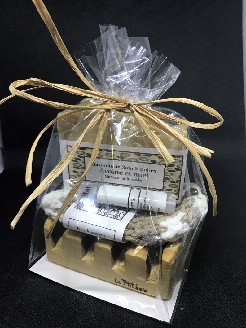 Puede incluir: Un set de regalo para el ba&ntilde;o y el cuerpo que incluye una pastilla de jab&oacute;n, un peque&ntilde;o tubo de loci&oacute;n, una toallita y un jabonera de madera. El jab&oacute;n est&aacute; envuelto en pl&aacute;stico transparente y atado con una cinta marr&oacute;n. El jab&oacute;n est&aacute; etiquetado con "Savonnerie Bain & Bulles Avoine et miel Savon &agrave; la soie". El tubo de loci&oacute;n est&aacute; etiquetado con "res ma beewax". La toallita es beige con un borde blanco. La jabonera est&aacute; hecha de madera marr&oacute;n claro y tiene las palabras "Le Ptit beis" grabadas en la parte inferior.