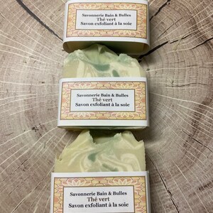 May include: Three bars of green and white soap with a label that reads "Savonnerie Bain & Bulles Th&eacute; vert Savon exfoliant &agrave; la soie".