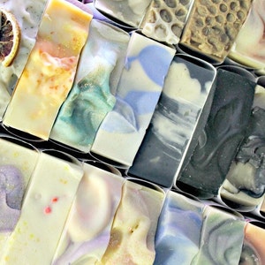 May include: A collection of handmade soap bars in various colours and patterns, including swirls, speckles, and embedded botanicals. The bars are arranged in rows and are ready to be used.
