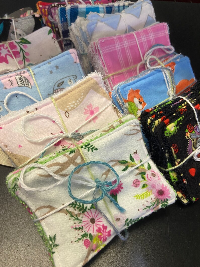 Op de afbeelding: Een set herbruikbare make-up remover pads, verpakt in stapels en vastgebonden met touw. De pads zijn gemaakt van zacht materiaal en hebben verschillende patronen, waaronder bloemen, dieren en geometrische ontwerpen.