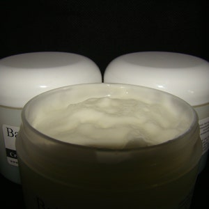 May include: Three white jars of body butter, two are closed and one is open, showing the white, creamy texture of the product.