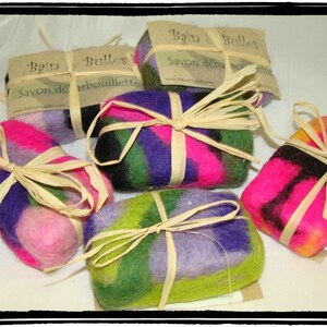 May include: Four colorful felted soap bars wrapped in natural twine. Each bar has a different pattern of pink, purple, green, and black wool. The bars are labeled "Bain de Bulles" and "Savon de la Bourbouillette".