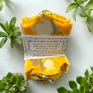 May include: A yellow and white swirl soap bar with a label that reads "Savonnerie Bain & Bulles Dragon chinois Avec argile et soie".