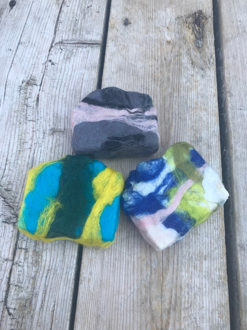 May include: Three felted soap bars in different colors and patterns. The soap bars are made of wool and have a soft, textured surface. The colors are blue, green, yellow, pink, and black.