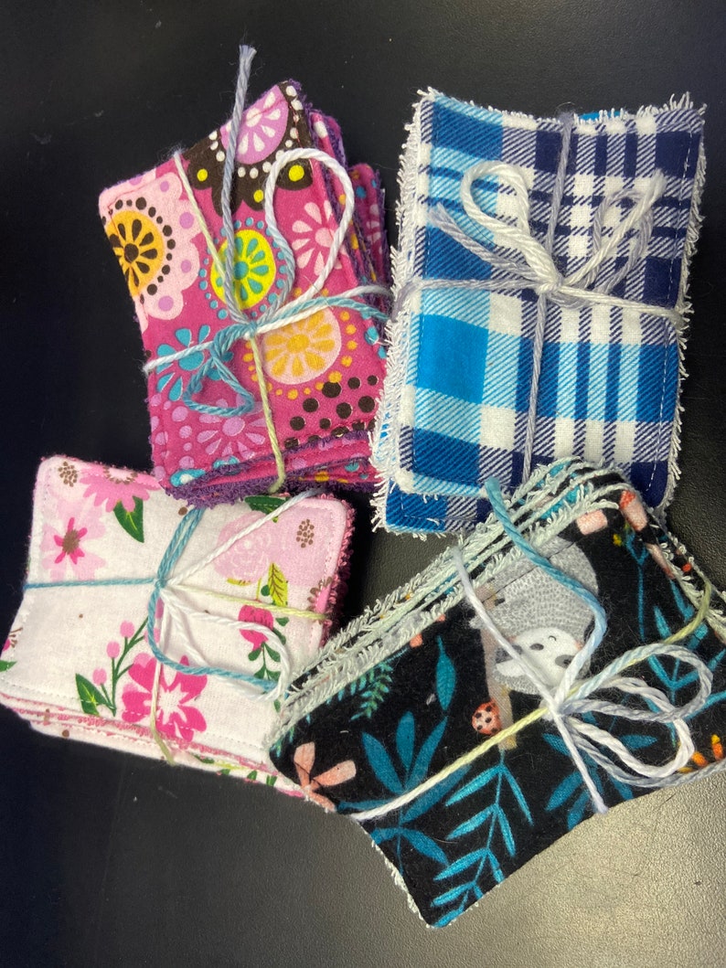 Op de afbeelding: Vier stapels herbruikbare make-up remover pads in verschillende stoffenpatronen. De pads zijn vastgebonden met touw en hebben bloemen-, ruit- en dierenprintontwerpen.