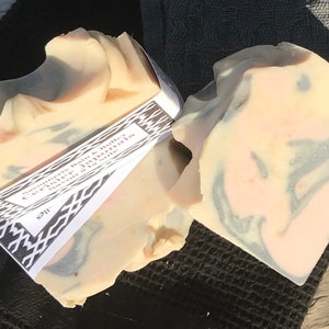 Puede incluir: Dos pastillas de jab&oacute;n rectangulares hechas a mano con un patr&oacute;n jaspeado en tonos crema, rosa suave y gris carb&oacute;n. Una etiqueta de papel blanco con bordes geom&eacute;tricos negros y el texto Savonnerie Bain & Bulles Cerisier Japonais envuelve el jab&oacute;n.