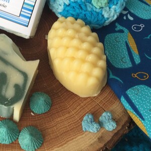 May include: A yellow, textured soap bar on a wooden surface with blue and white decorative items.