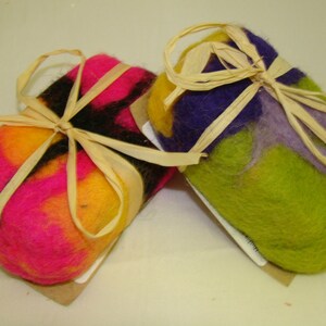 May include: Two handmade soap bars wrapped in natural twine. One bar is pink, yellow, and black, and the other is green, purple, and yellow.