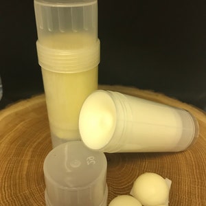 May include: Three clear plastic containers with white cream inside. Two containers are upright and one is lying on its side. Three small white balls of cream are on a wooden surface.