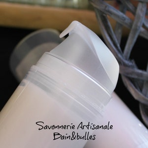 May include: A white cylindrical cosmetic pump bottle with a translucent cap. The bottle features black printed text that reads Savonnerie Artisanale Bain&bulles. The pump mechanism is made of a semi-transparent white plastic material.