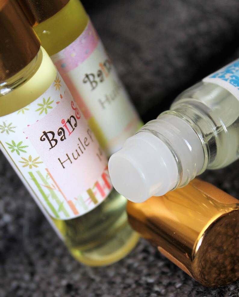 May include: Three glass bottles with gold caps and labels. The labels are white with pink and green floral designs. The text on the labels reads "Bain & Huile" and "Bain".