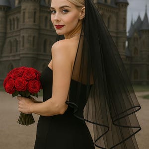 May include: A woman in a black dress and veil holds a bouquet of red roses. The black veil has a delicate trim. The background features a large stone building with multiple turrets.