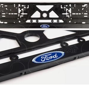 Op de afbeelding: Zwarte kentekenplaathouder met het Ford-logo in blauw en wit. De houder heeft een rechthoekige vorm met diverse uitsparingen voor montage. Het Ford-logo staat prominent onderaan.