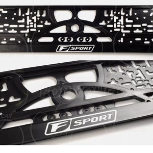 Pode incluir: Moldura preta para placa de carro com design geométrico e texto branco "F SPORT". A moldura tem recortes e furos de montagem. Projetada para um veículo.