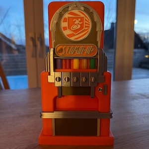 Peut inclure: Distributeur automatique de style vintage orange et argent avec le texte "STAMIN-UP" et un logo représentant une personne courant avec un cercle autour.