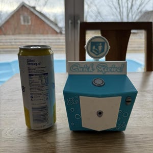 May include: A blue and white Quick Revive vending machine replica featuring a circular top sign, a central white panel, and text reading Ice Cold and Sold Here, positioned next to a 330ml Bonaqua beverage can for a clear sense of scale.