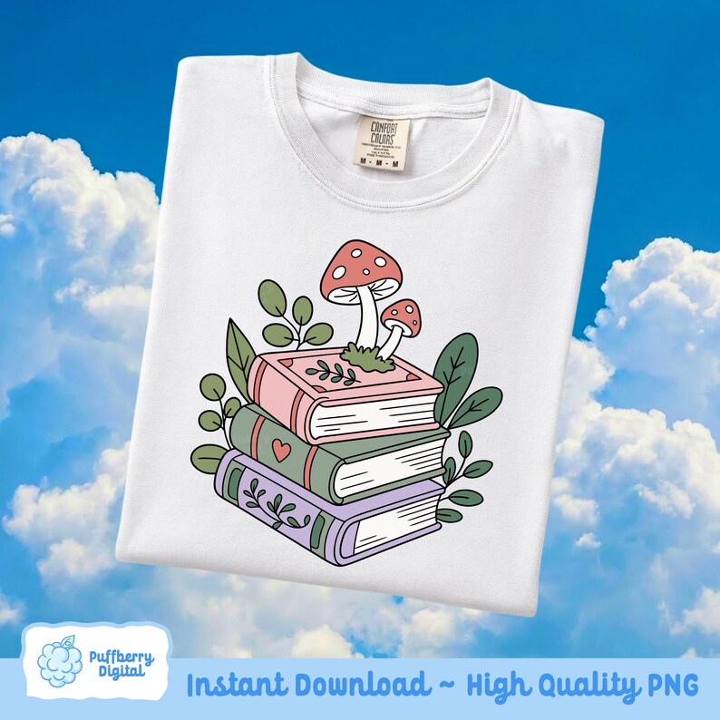 May include: White sweatshirt featuring a stack of three books with a mushroom and leaf design. The books are pink, green, and purple, with decorative details. The sweatshirt has a Comfort Colors tag.