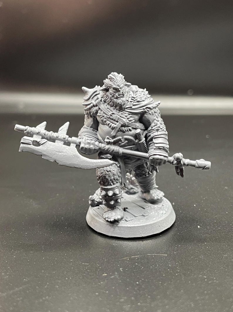 May include: A gray plastic miniature figurine of a furry, humanoid creature holding a large axe. The creature has a fierce expression and is wearing armor and a cloak. The figurine is standing on a round base.