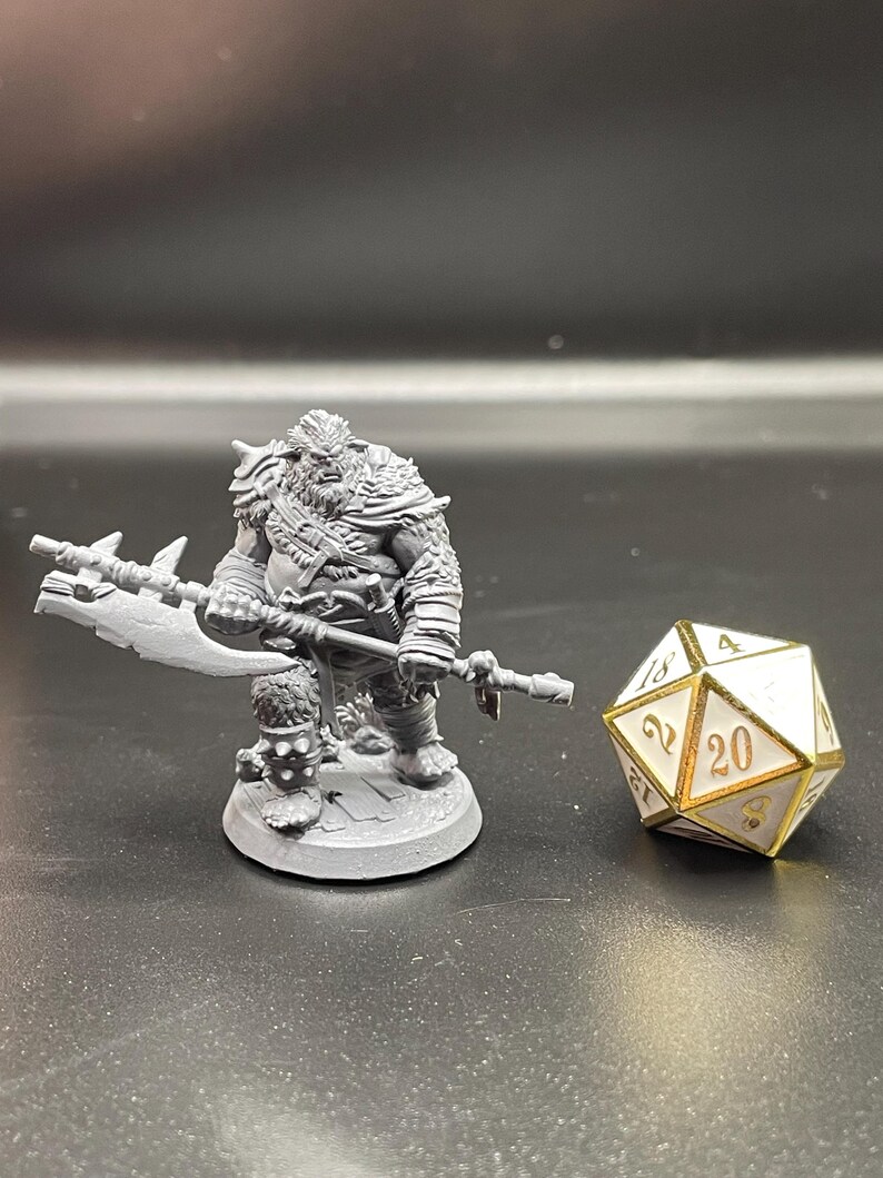 May include: A gray plastic miniature figurine of a warrior holding a large axe. The figurine is standing on a round base. A white 20-sided die with gold accents is in the background.