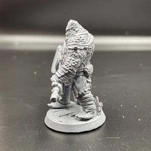 May include: A gray, unpainted miniature figurine of a furry, humanoid creature holding an axe. The figure is standing on a round base.