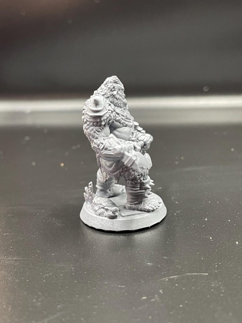 May include: A gray plastic miniature figurine of a furry, humanoid creature holding a weapon. The figure is standing on a round base.