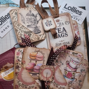 May include: A selection of vintage-style tags with brown ribbon detailing. The tags display illustrations of teacups, teapots, and macarons. Some tags have the text "Tea Bags" and "Lollies Printables". The color scheme includes cream, pink, and brown.