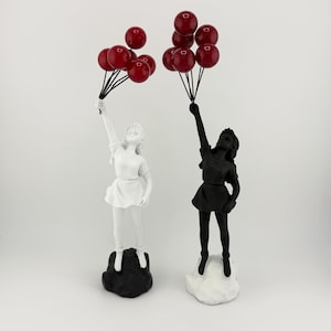 Puede incluir: Dos esculturas de niños sosteniendo globos rojos. Una escultura es blanca y la otra es negra.