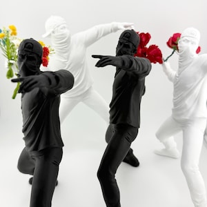 Puede incluir: Tres figuras estilizadas, cada una con una máscara y una gorra, sostienen flores. Una figura es negra, y las otras dos son blancas.