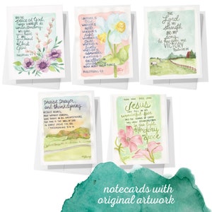 May include: Set of five watercolor notecards with inspirational quotes and floral illustrations. The cards feature quotes from the Bible, including "And the peace of God...", "Whatever is true...", "Praise, prayer, and thanksgiving...", "Turn your eyes upon Jesus...", and "The Lord is my strength..." Each card has a different floral design, including pink and purple flowers, white flowers, and green foliage.