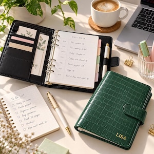 May include: A dark green crocodile-textured personal planner with the name LISA embossed in gold on the cover. The open planner features a weekly schedule, multiple card slots, and a gold ring binder. A separate spiral-bound to-do list notebook and a white and gold pen are included.